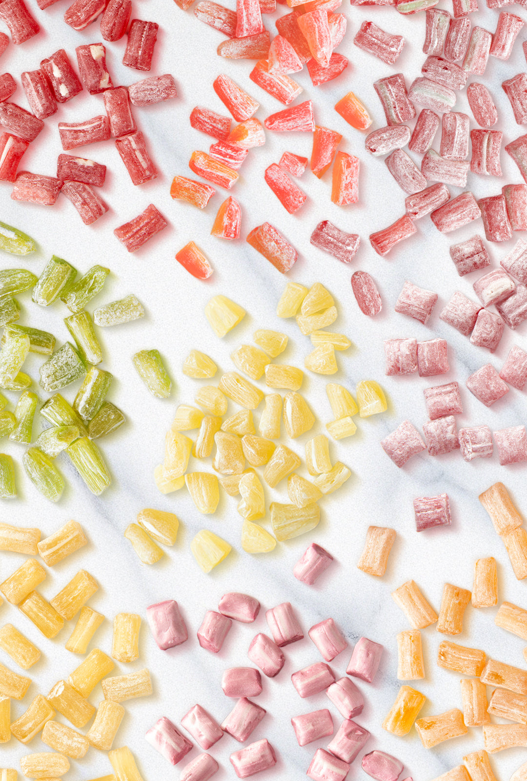 Assorted Butterfields Candy pieces in various flavors, including Peach, Cinnamon, Ginger, Key Lime, Lemon, Honeybell Orange, Cherry, Muscadine Grape, and Watermelon, arranged on a white marble surface. The candies have a glossy, sugar-dusted coating and come in vibrant colors, reflecting their unique flavors.